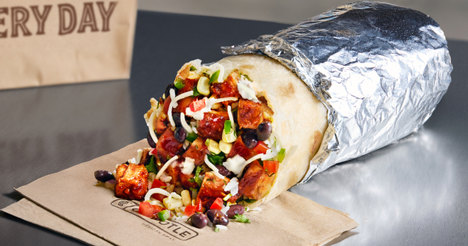 A close up point of view photo of a Chipotle Honey Chicken Burrito wrapped in foil and filled with white rice, black beans, freshly grilled Chipotle Honey Chicken, fresh tomato salsa, and roasted chili corn salsa.